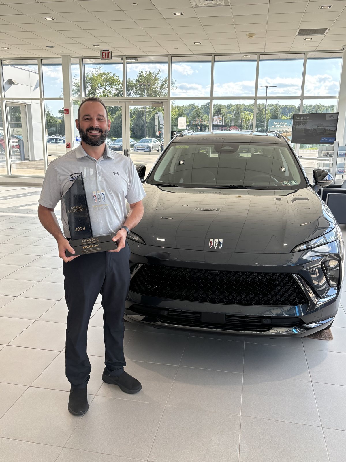 Nate of Crivelli Chevrolet Buick holding the Buick GM Mark of Excellence award in the Mount Pleasant showroom