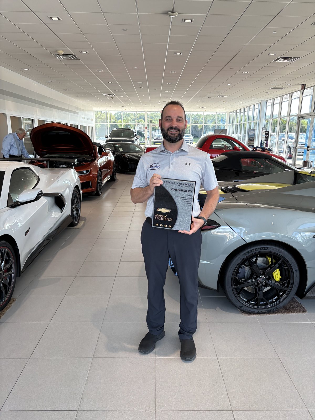 Nate of Crivelli Chevrolet Buick holding the Chevrolet GM Mark of Excellence award in the Mount Pleasant showroom